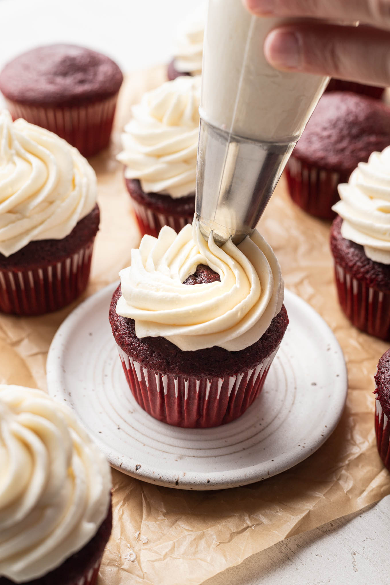 Boiled ermine frosting being piped onto a red velvet cupcake. 