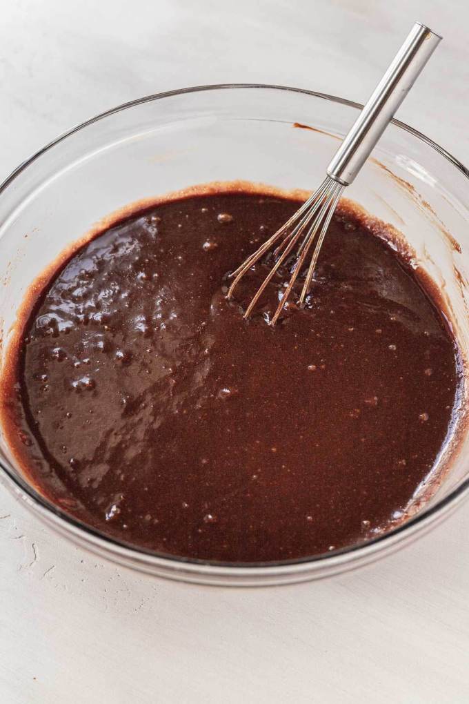 A glass mixing bowl full of cake batter. A whisk rests on the side.