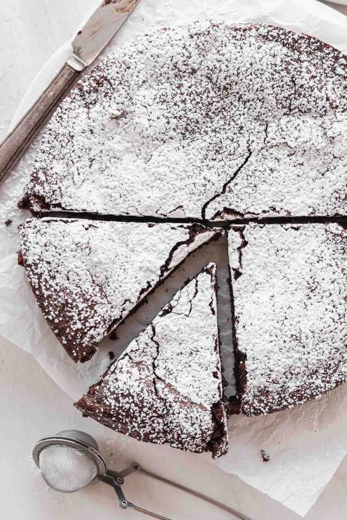 An overhead view of a flourless chocolate cake dusted with powdered sugar. Two slices have been cut. 