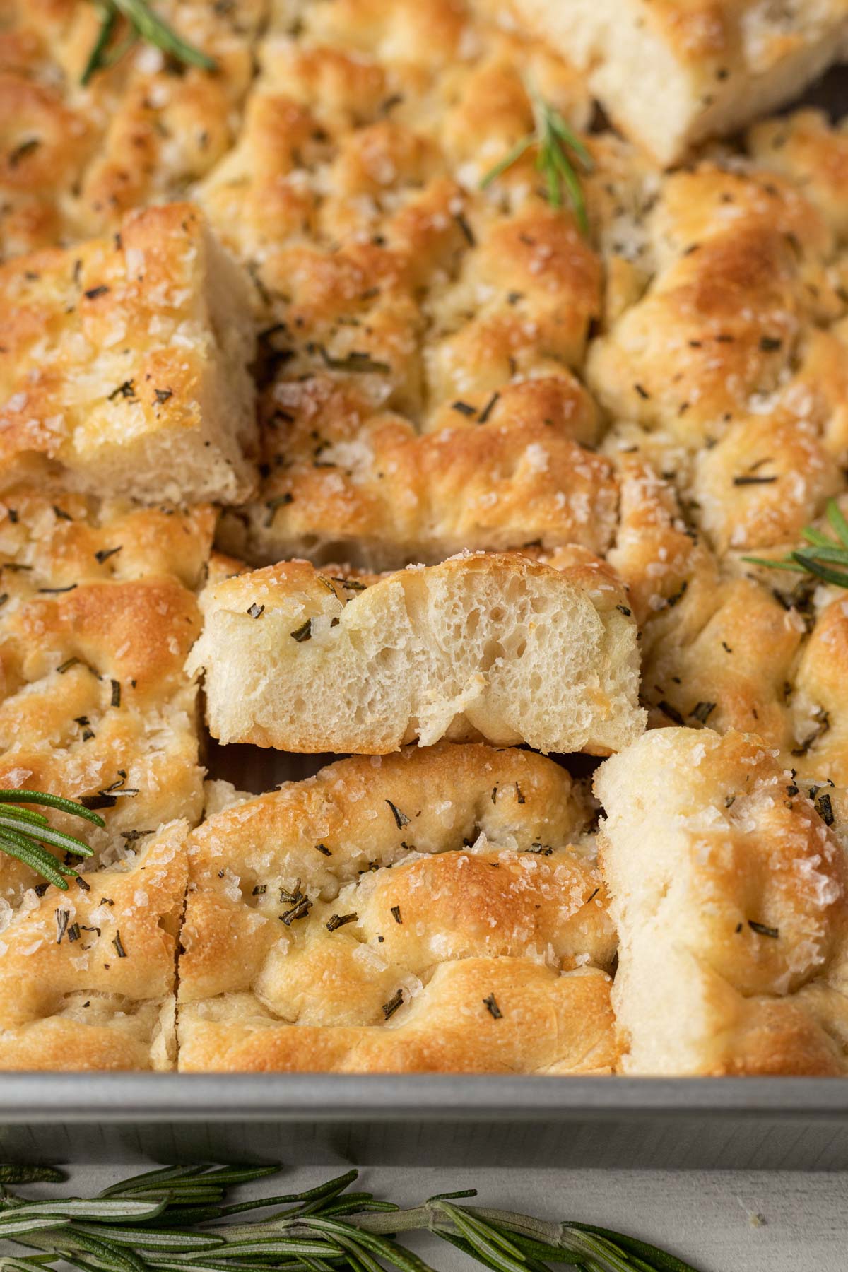 Slices of rosemary focaccia in a metal baking pan. Some slices are turned on their sides. 