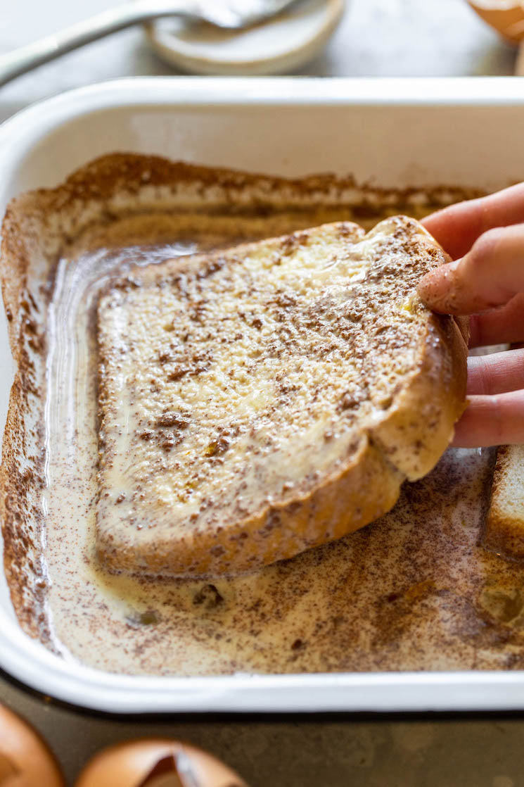 A piece of bread being dipped into the egg mixture showing how it should be covered completely and soaked into the bread.