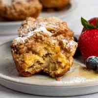 Two French toast muffins on a plate with fresh fruit. The muffin in the front has a bite missing.