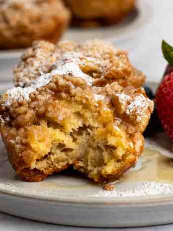 Two French toast muffins on a plate with fresh fruit. The muffin in the front has a bite missing.