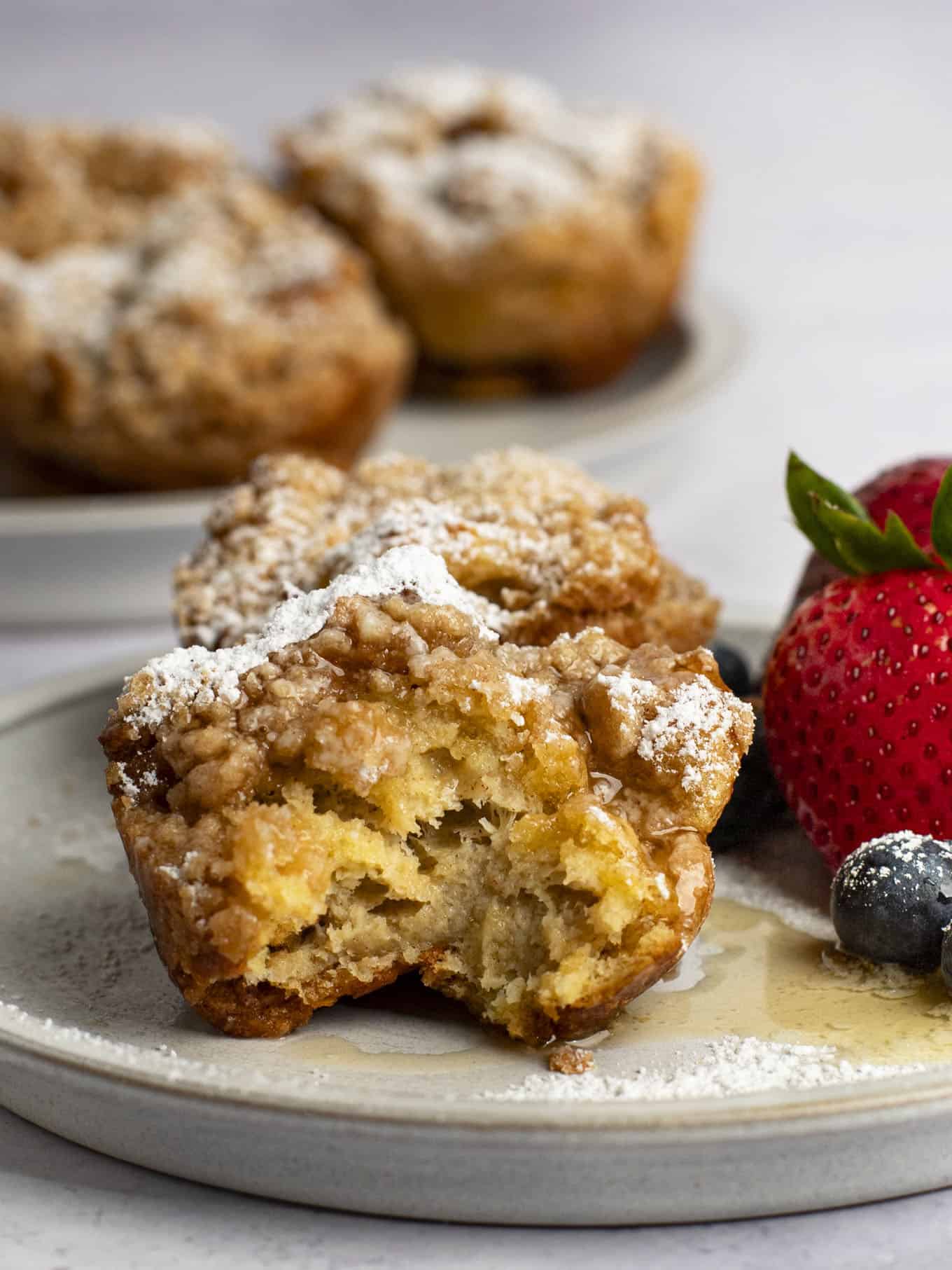 Two French toast muffins on a plate with fresh fruit. The muffin in the front has a bite missing.