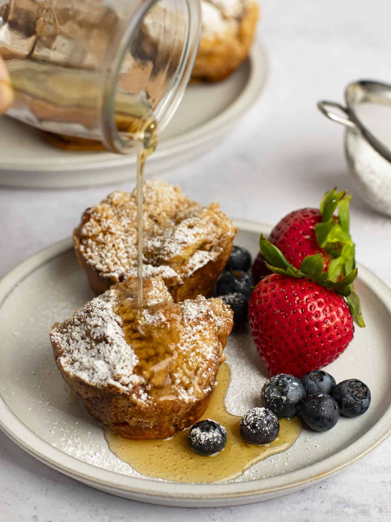 Maple syrup being poured on top of French toast muffins on a plate.