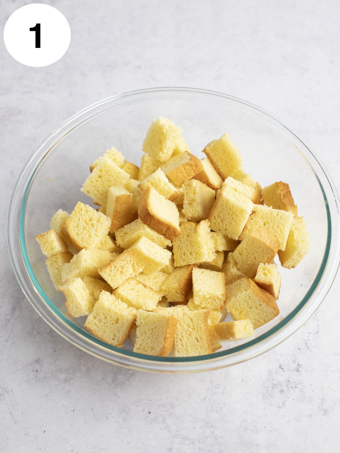 Cubed bread in a large glass mixing bowl.