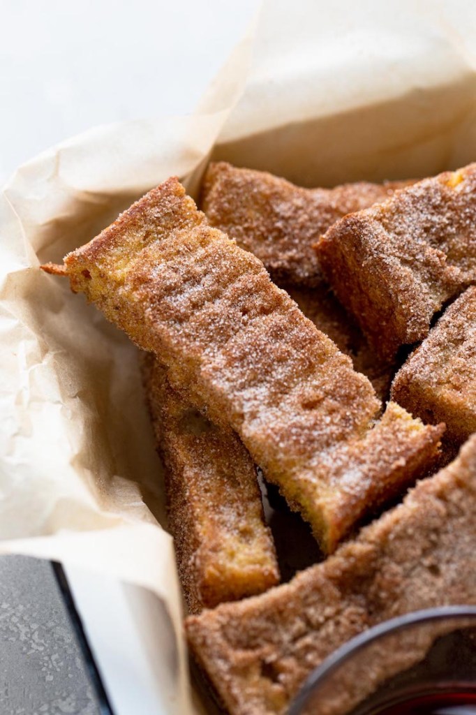 A pile of cinnamon french toast sticks in a baking dish lined with parchment paper. 