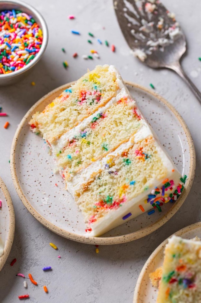 A slice of funfetti layer cake on a speckled white plate. 