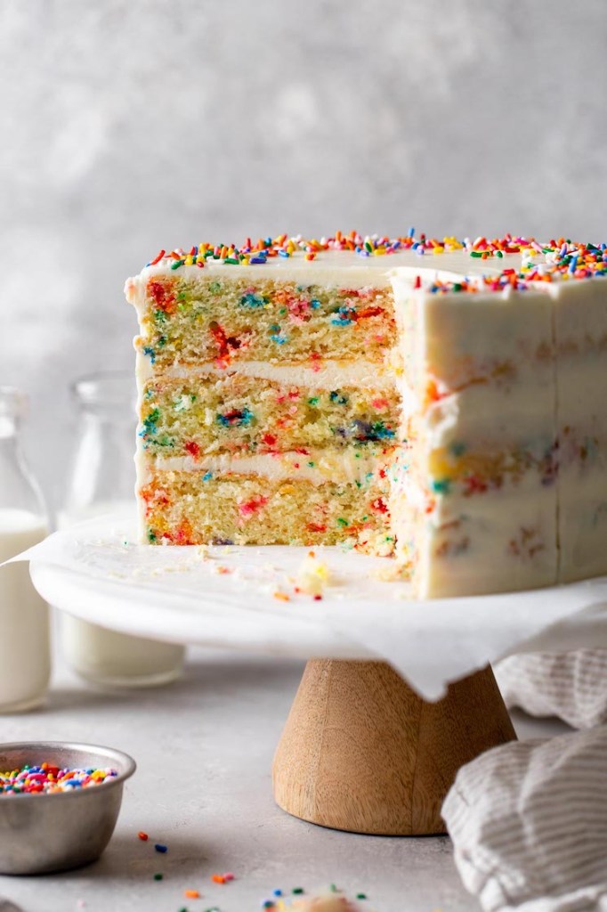 A funfetti birthday cake that's been sliced on a cake stand. 