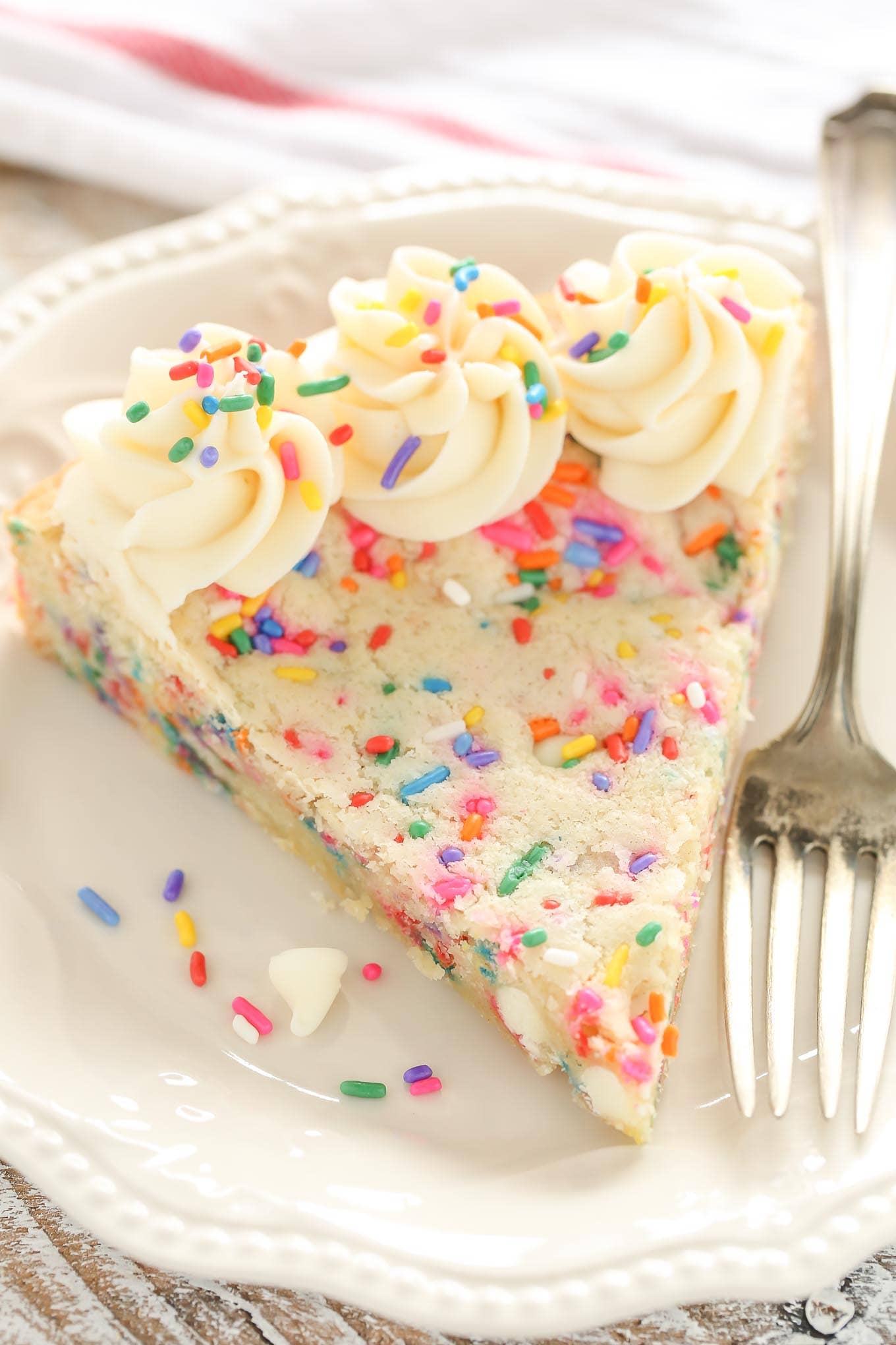 A slice of funfetti sugar cookie cake on a white plate with a fork. 