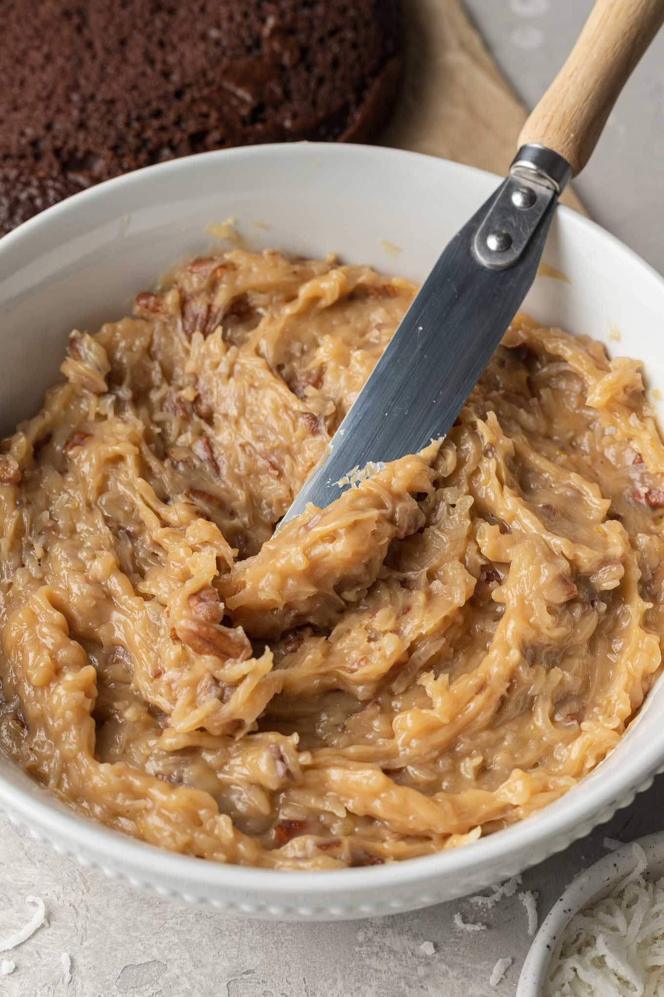 A large bowl of German chocolate cake frosting with an offset spatula. 