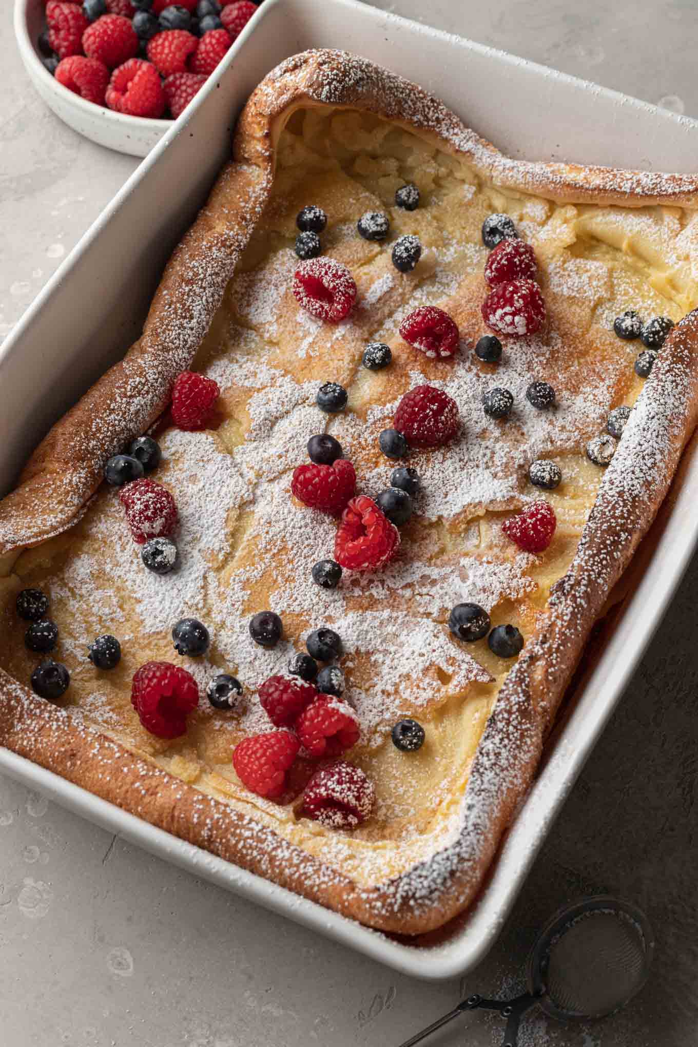 A baked German pancake dusted with powdered sugar and topped with fresh berries. 