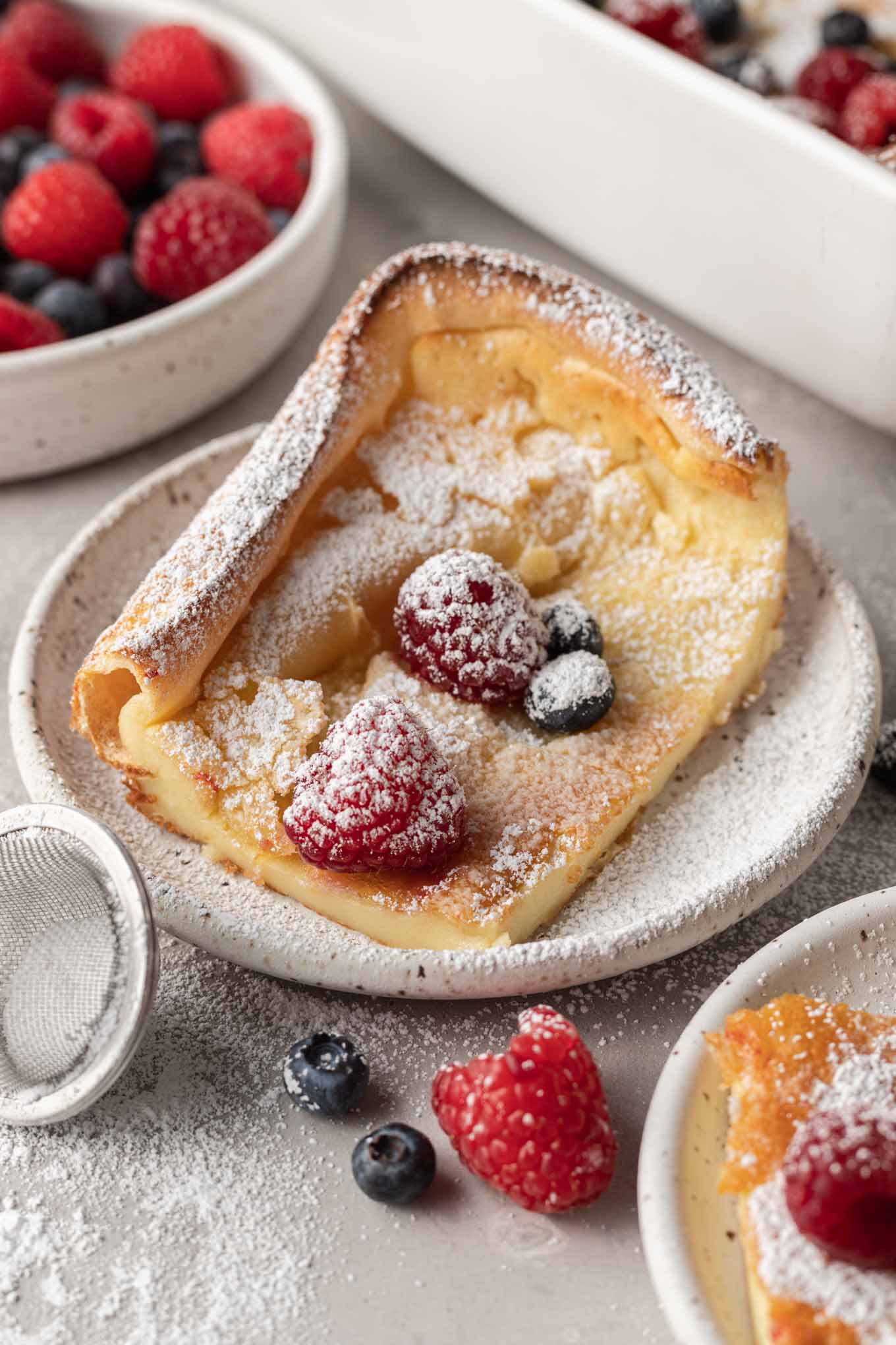 A serving of German pancakes on a plate, topped with powdered sugar and fresh berries. 