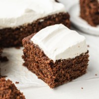 A slice of gingerbread cake topped with homemade whipped cream. The rest of the cake is in the background.