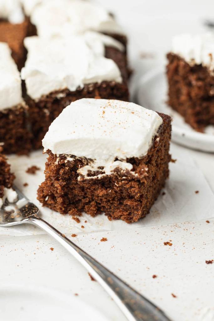 Slices of spiced molasses cake topped with whipped cream. A fork rests on the side. 