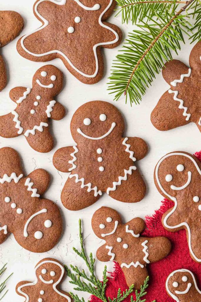 An overhead view of homemade gingerbread cookies topped with icing, with pine branches scattered around. 