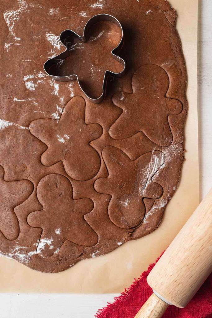 An overhead view of gingerbread cookie dough being cut out with a cookie cutter. 