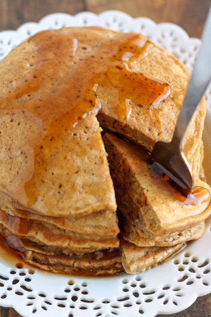 Stack of gingerbread pancakes on a white plate. A bite has been cut out. 