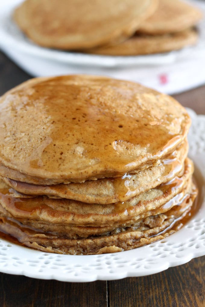 A stack of gingerbread pancakes on a white plate. More pancakes rest in the background. 