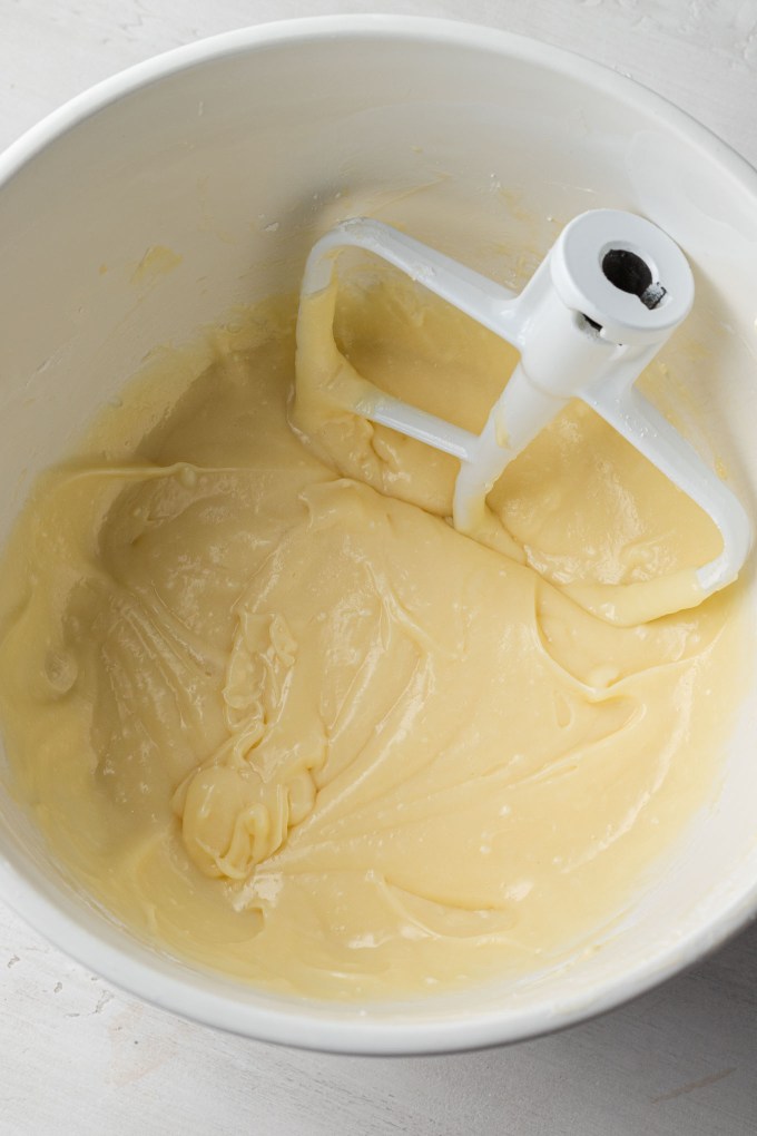 An overhead view of a sweetened cream cheese mixture in a white mixing bowl with a paddle attachment.