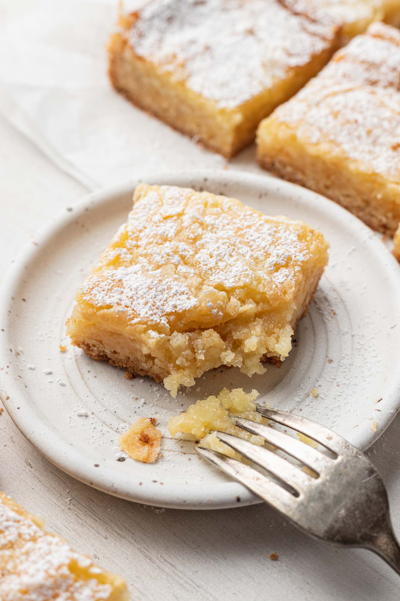 A slice of ooey gooey butter cake on a dessert plate, with a bite missing. 