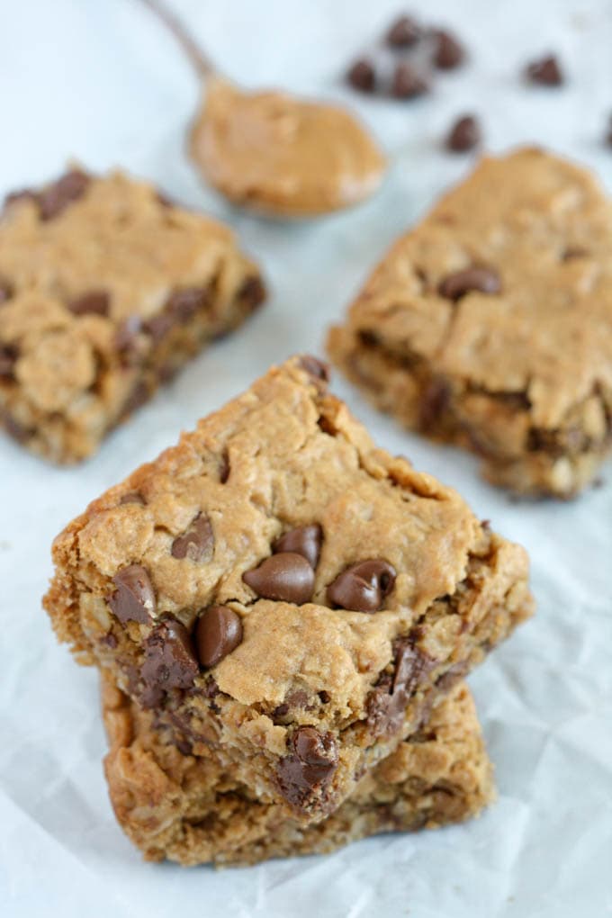 Four oatmeal breakfast bars next to a spoonful of peanut butter and a handful of chocolate chips. 