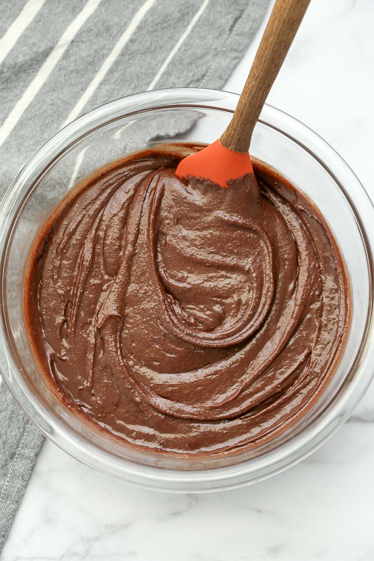 A clear bowl filled with homemade brownie batter and a rubber spatula.