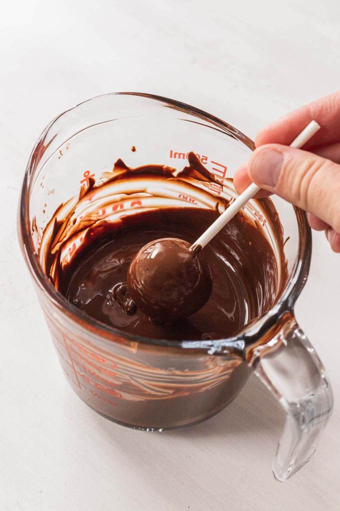 A cake pop being dunked into a glass of melted chocolate.