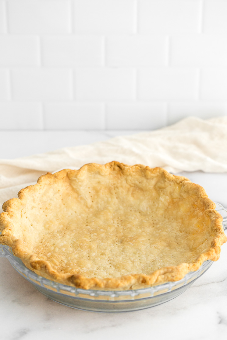 A homemade pie crust in a pie dish sitting on top of a marble surface.