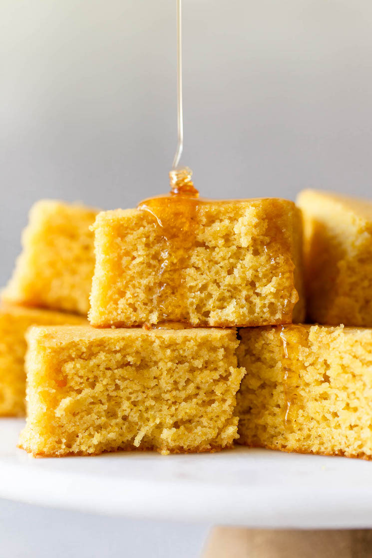 A stack of cornbread on a marble cake stand topped with honey.