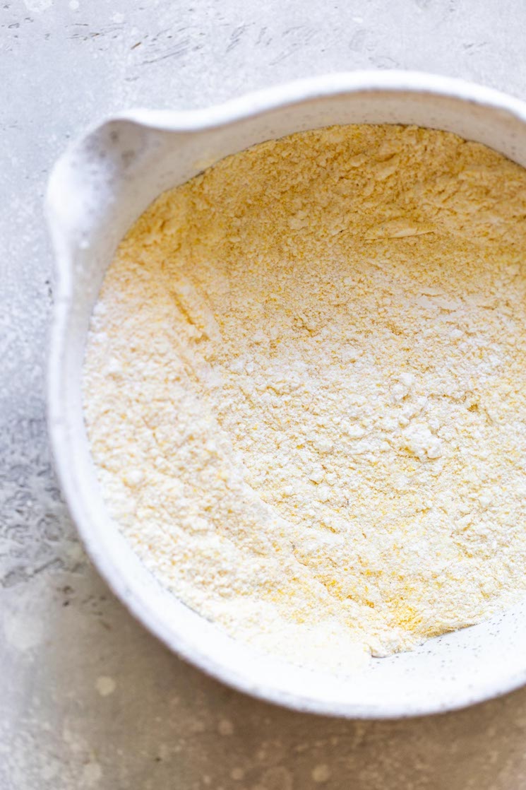 The dry ingredients needed to make cornbread in a rustic white speckled clay bowl.