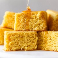 A stack of square cornbread slices with honey being drizzled on top.