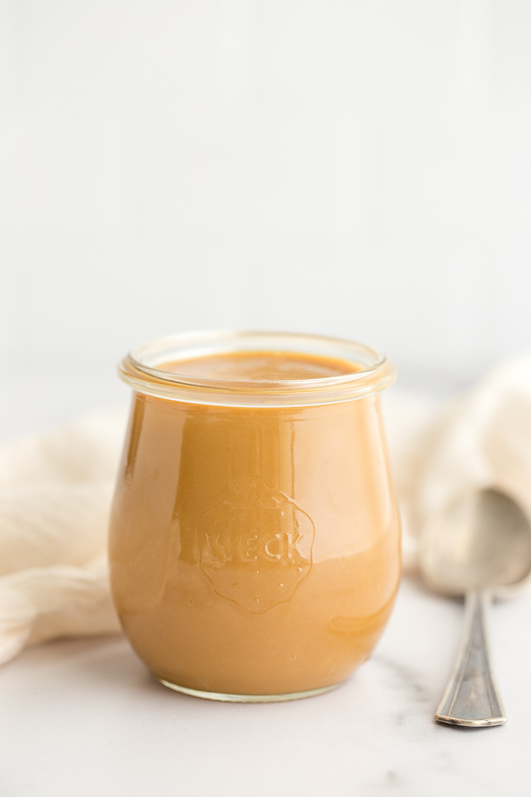 A glass jar of dulce de leche sitting on a marble surface. 