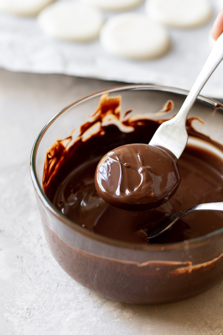 A glass bowl filled with melted chocolate and peppermint patty dough being dipped into it with a fork.