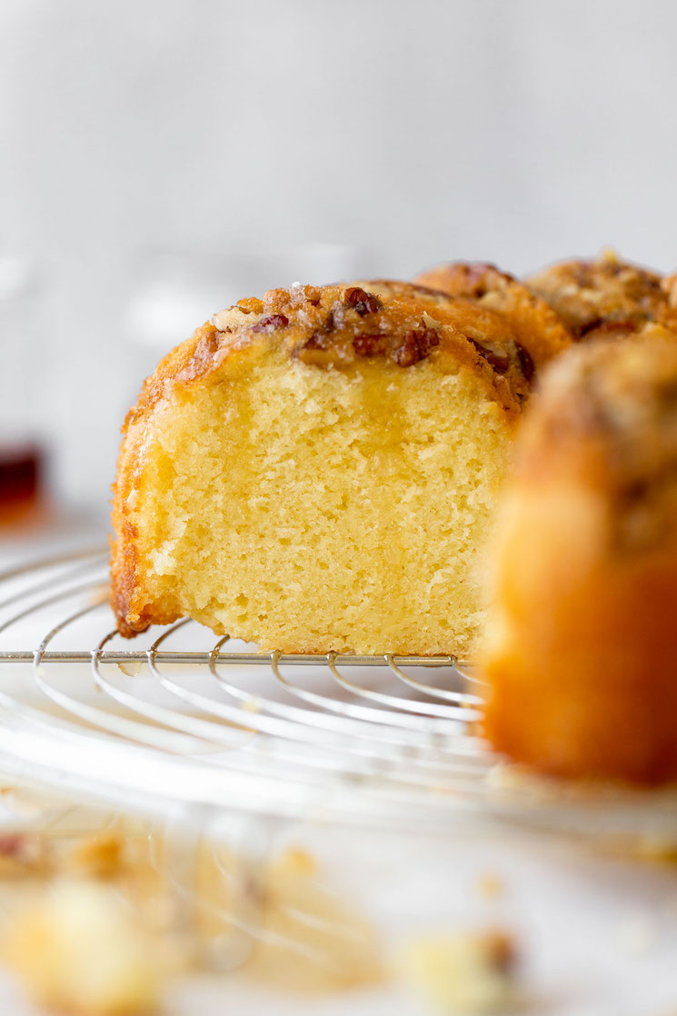 A finished rum cake resting on a round cooling rack with a slice cut out to show the cake texture.