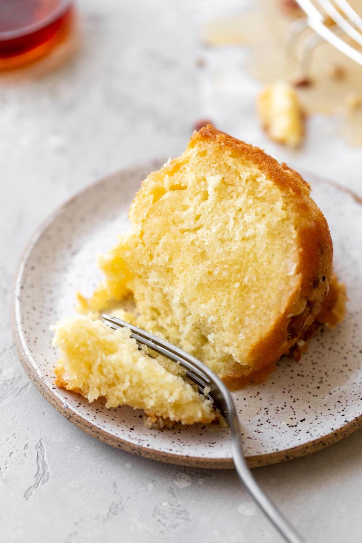 A single slice of cake on a rustic clay plate and a bite taken out with a fork.