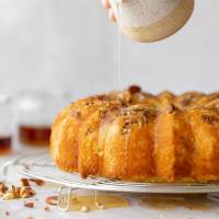 A baked rum cake resting on a round cooling rack and the rum glaze being poured over the top.