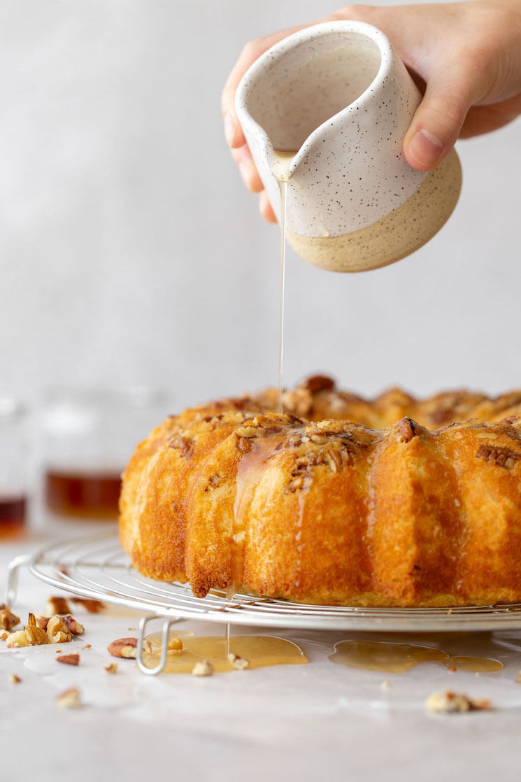 A baked rum cake resting on a round cooling rack and the rum glaze being poured over the top.