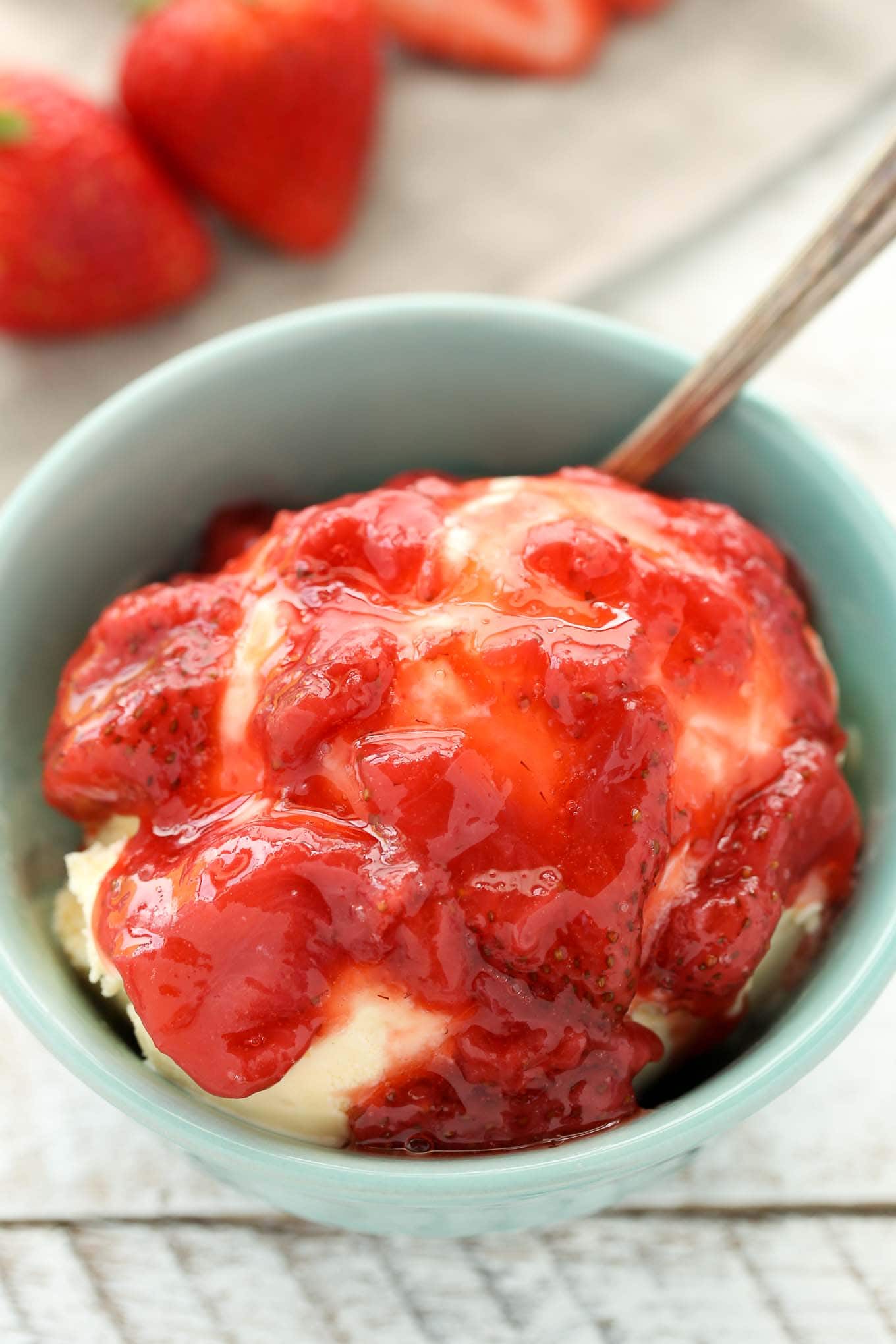 A bowl of ice cream topped with strawberry sauce. Fresh berries are lined up in the background. 