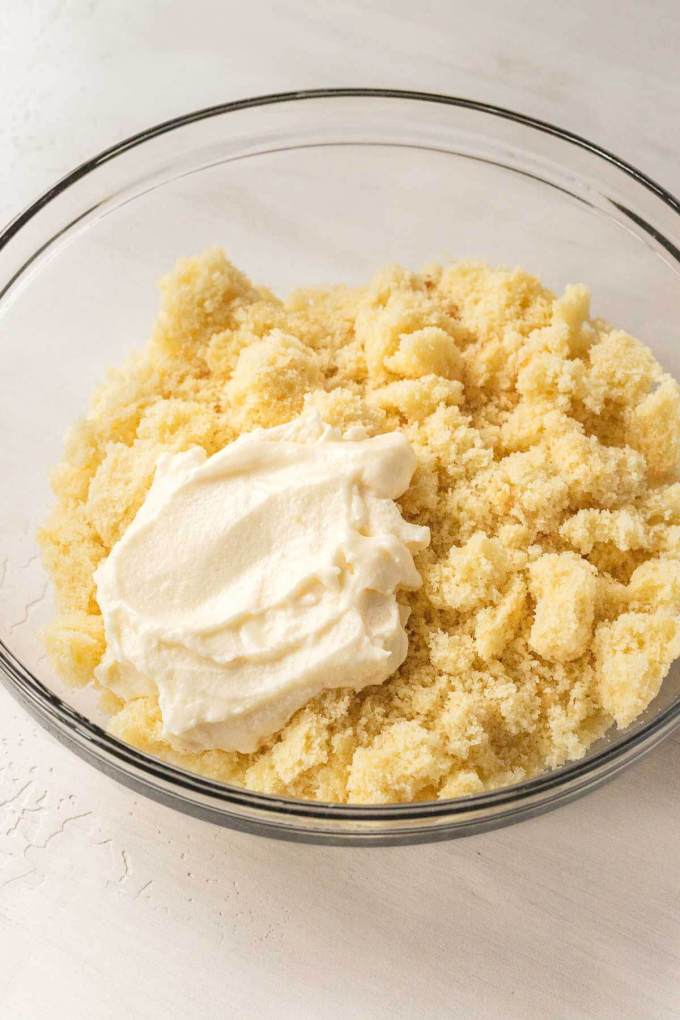 Crumbled vanilla cake in a glass bowl with a dollop of buttercream frosting on top.