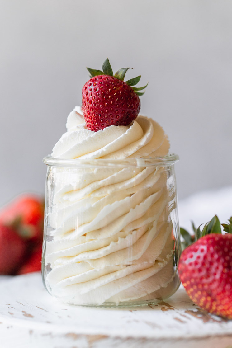 A small glass jar filled with homemade whipped cream topped with a strawberry.