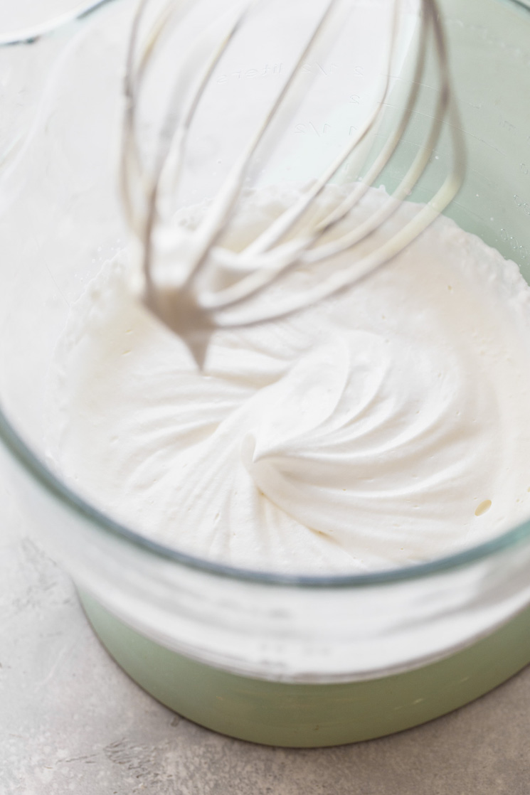 Whipped cream mixed to stiff peaks in a glass mixing bowl.