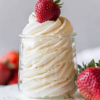 A small glass jar filled with whipped cream and topped with a strawberry.