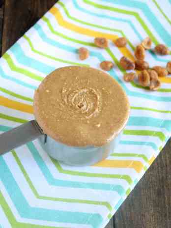 A measuring cup of honey peanut butter on a striped towel.