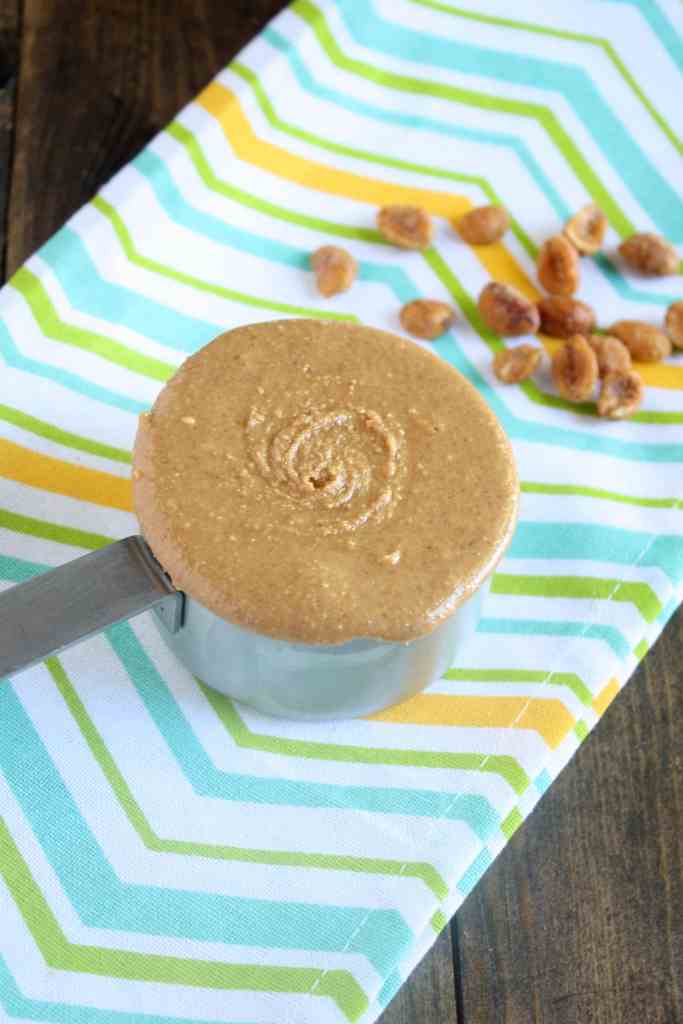 A measuring cup of honey peanut butter on a striped towel. 