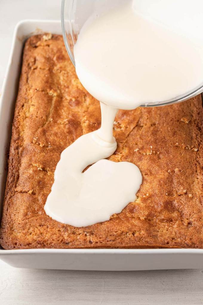 A process shot showing vanilla icing being poured over a baked cinnamon swirl cake.