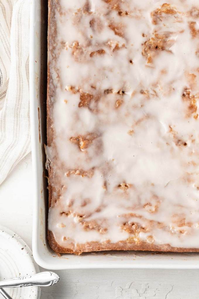 An overhead view of an iced honey bun cake in a white baking dish.