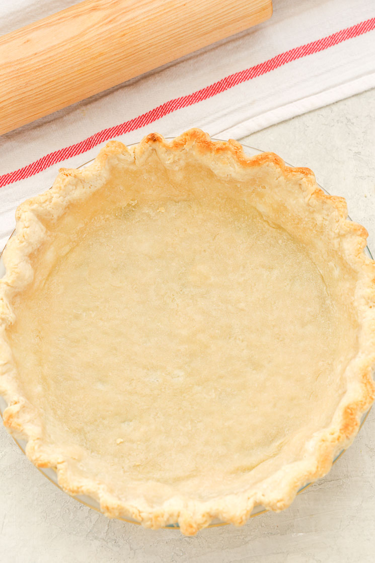 A partially baked pie crust next to a striped towel and rolling pin.