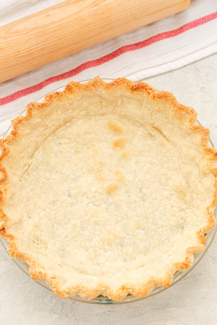 A partially baked pie crust next to a wood rolling pin on a striped towel. 