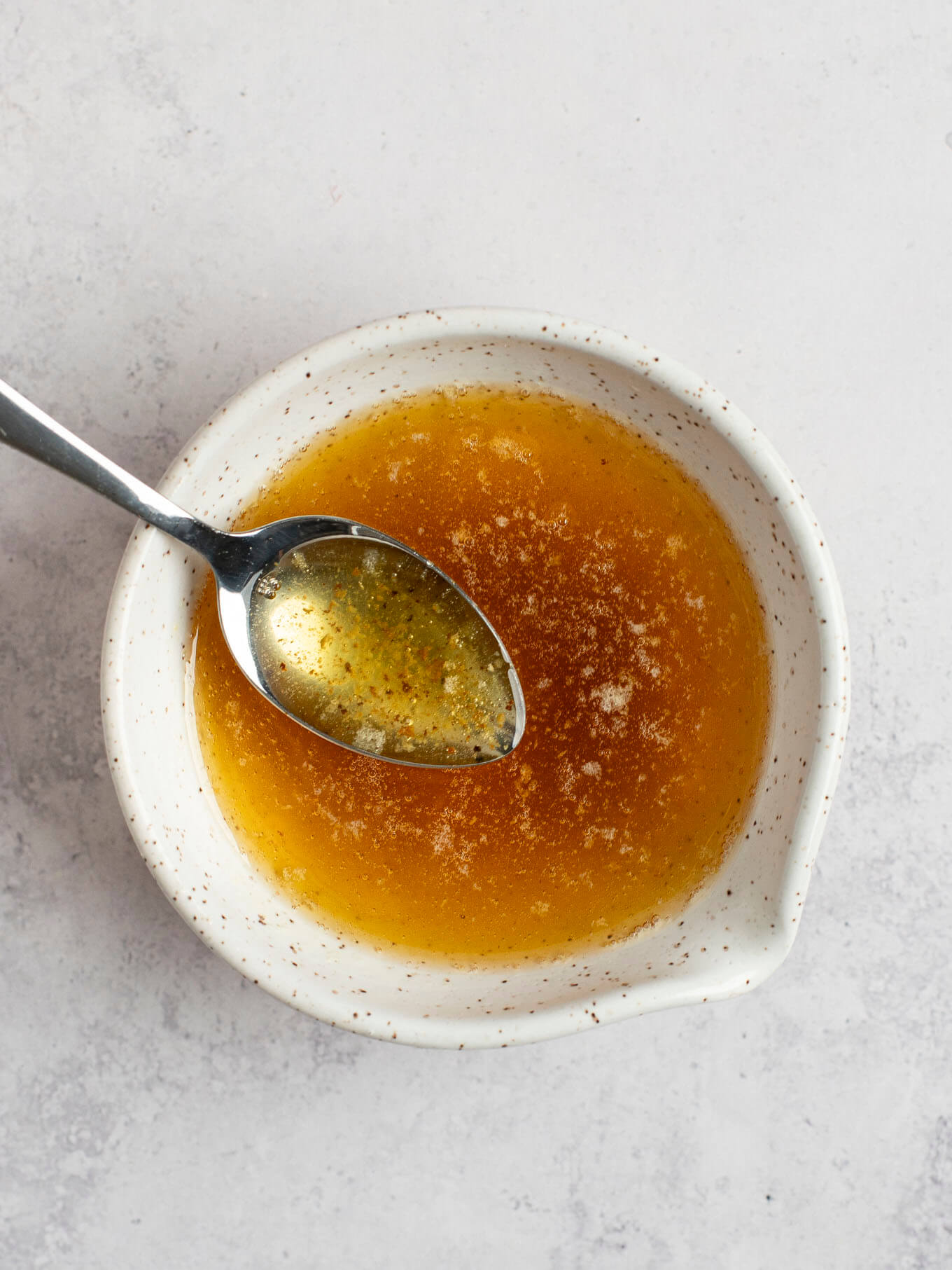 A small speckled white bowl filled with browned butter. A spoon is resting inside of the bowl of melted butter.